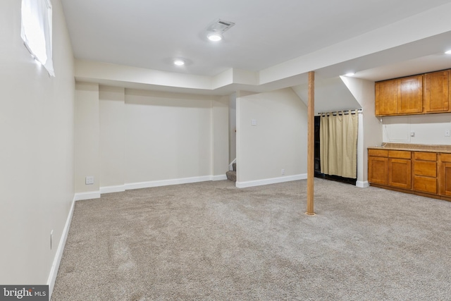 finished below grade area featuring visible vents, baseboards, stairway, light carpet, and recessed lighting