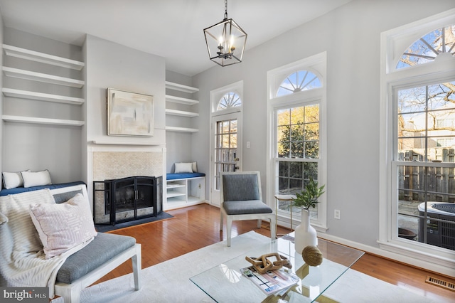 living area featuring a notable chandelier, wood finished floors, visible vents, and a tile fireplace