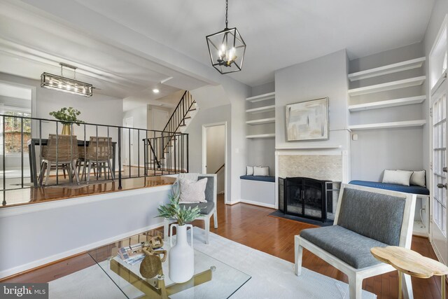 living room featuring a fireplace with flush hearth, wood finished floors, an inviting chandelier, baseboards, and stairs