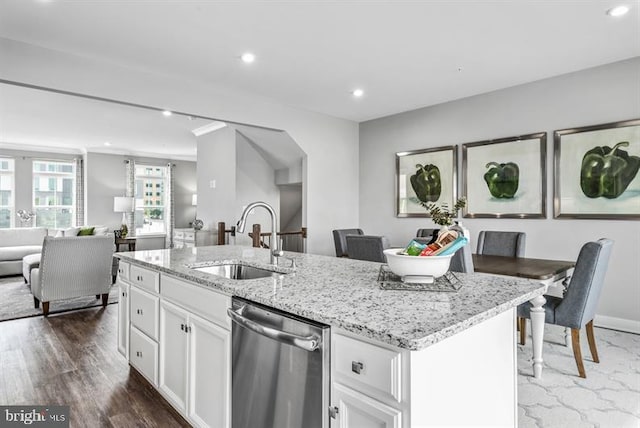 kitchen with sink, dishwasher, light stone countertops, white cabinets, and a center island with sink