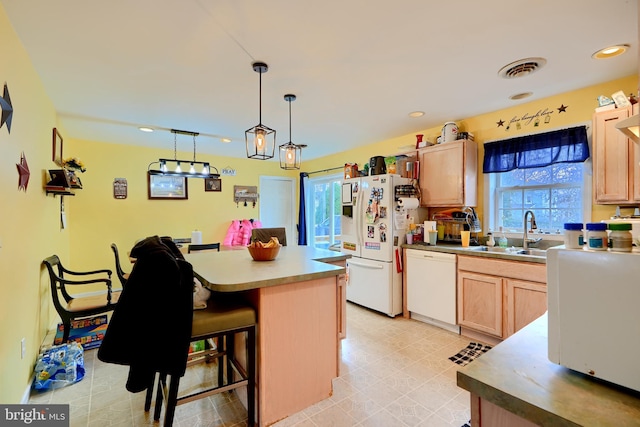 kitchen featuring decorative light fixtures, light brown cabinets, a kitchen island, a sink, and white appliances