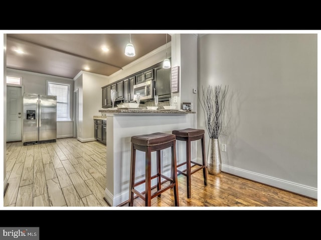 kitchen with a kitchen bar, light hardwood / wood-style floors, stainless steel appliances, kitchen peninsula, and ornamental molding