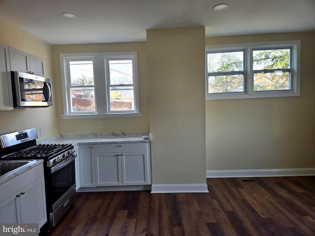 kitchen with appliances with stainless steel finishes, light stone counters, white cabinets, and dark hardwood / wood-style flooring