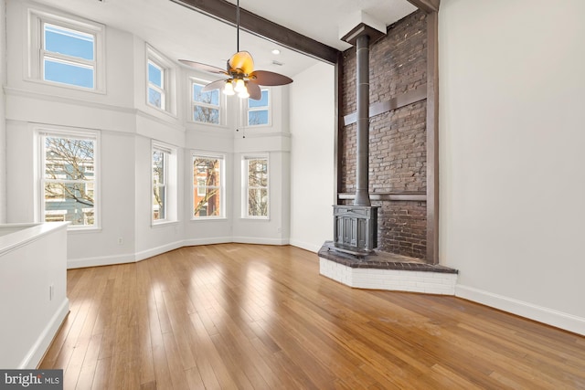 unfurnished living room with baseboards, a towering ceiling, a wood stove, light wood-style floors, and beam ceiling