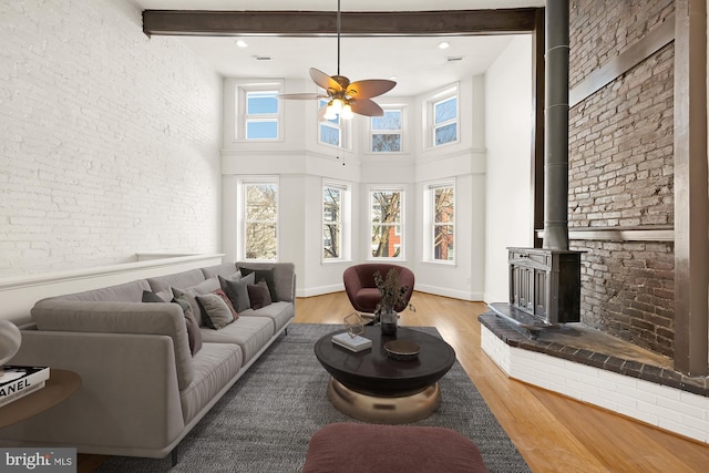 living area with light wood finished floors, a towering ceiling, a wood stove, and a ceiling fan