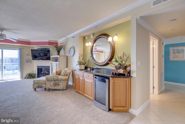 interior space featuring crown molding, visible vents, a glass covered fireplace, a textured ceiling, and beverage cooler