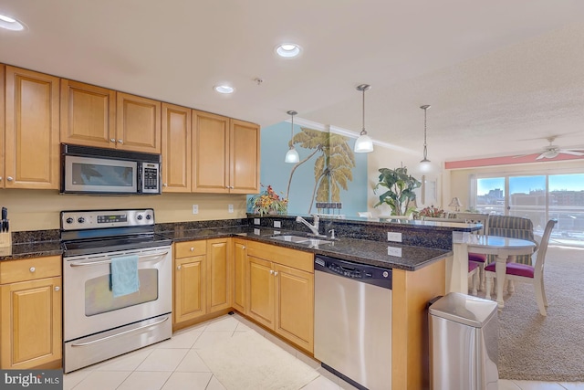 kitchen featuring stainless steel appliances, a peninsula, a sink, dark stone countertops, and decorative light fixtures