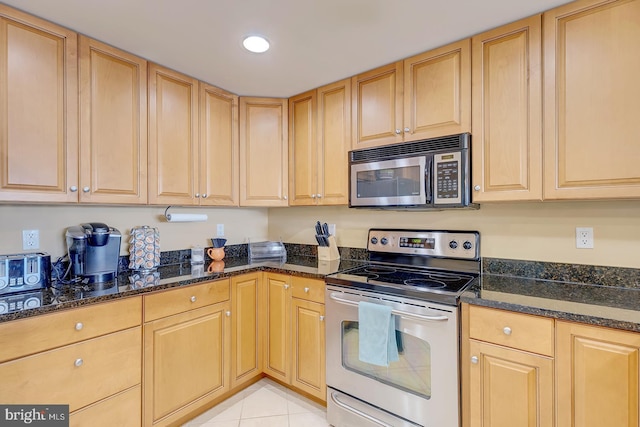 kitchen with stainless steel appliances, light brown cabinetry, and dark stone countertops