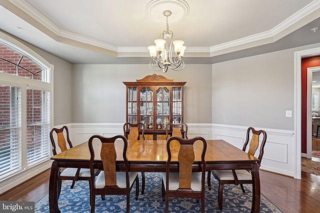 dining area featuring a chandelier, a tray ceiling, a wainscoted wall, and dark wood finished floors