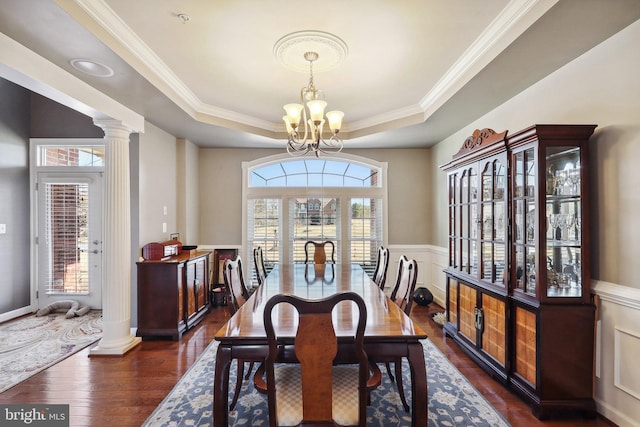 dining area featuring a notable chandelier, a raised ceiling, dark wood finished floors, and ornate columns