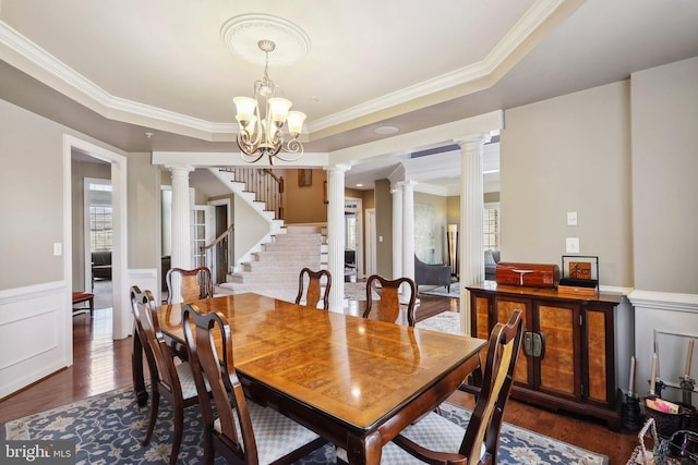 dining space featuring ornate columns, a raised ceiling, dark wood-type flooring, and wainscoting