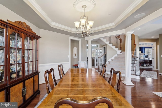 dining space with a raised ceiling, an inviting chandelier, wood finished floors, ornate columns, and stairs