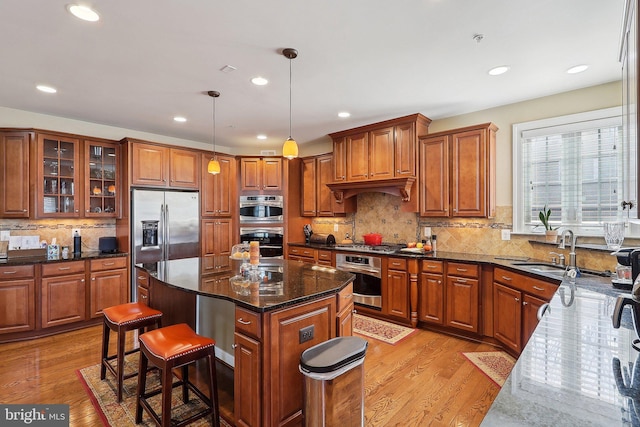 kitchen featuring light wood finished floors, appliances with stainless steel finishes, brown cabinetry, and a sink