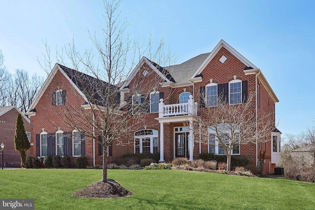 colonial home with a balcony, a front yard, central AC, and brick siding