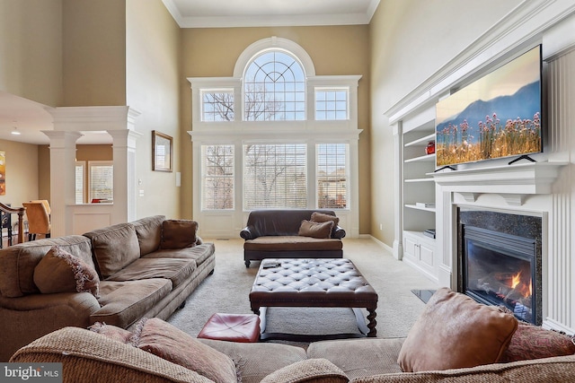 living room with carpet floors, baseboards, ornamental molding, a glass covered fireplace, and decorative columns