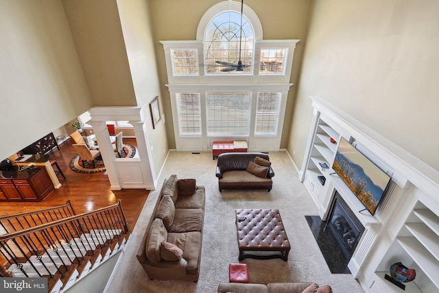 living area featuring a fireplace with flush hearth, a healthy amount of sunlight, decorative columns, and a towering ceiling