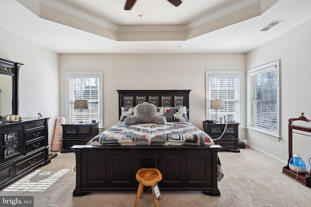 bedroom featuring light carpet, visible vents, baseboards, ornamental molding, and a tray ceiling