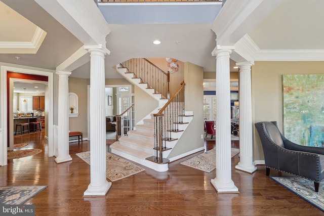 foyer entrance with ornate columns, stairway, ornamental molding, and wood finished floors