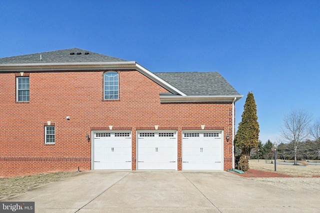 view of side of home with a garage, driveway, brick siding, and a shingled roof