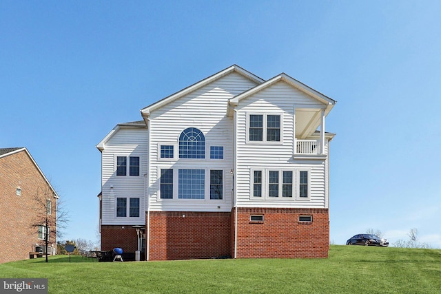 back of property with brick siding, a lawn, and a balcony