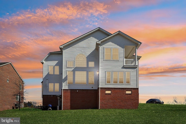 view of front facade featuring brick siding, a balcony, and a front lawn