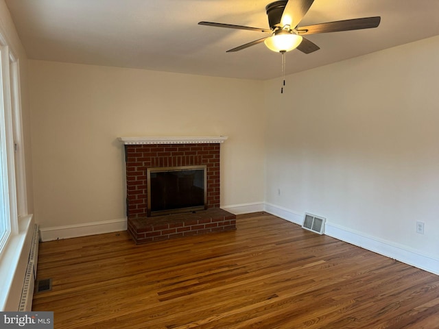 unfurnished living room with a brick fireplace, dark hardwood / wood-style floors, ceiling fan, and baseboard heating