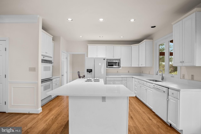 kitchen with white appliances, white cabinets, a kitchen island, and a sink