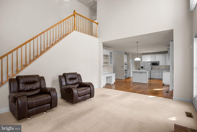 carpeted living room with visible vents, wood finished floors, baseboards, a towering ceiling, and stairs