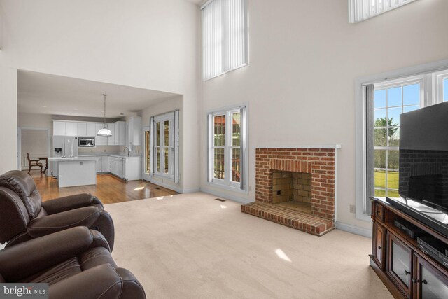 living area featuring a brick fireplace, baseboards, a towering ceiling, and light carpet