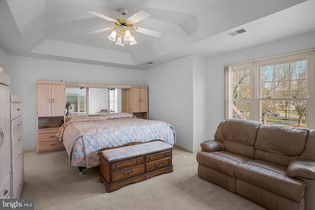 bedroom with visible vents, light carpet, a tray ceiling, baseboards, and ceiling fan