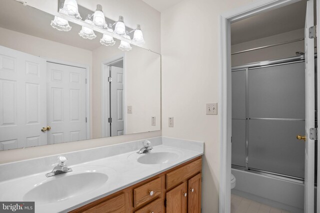 bathroom with double vanity, toilet, enclosed tub / shower combo, and a sink