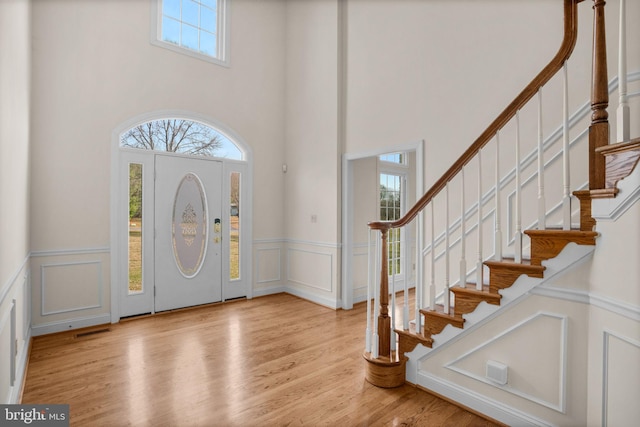 entrance foyer featuring light wood finished floors, a decorative wall, stairs, and visible vents