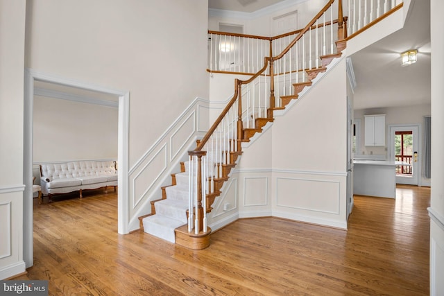 stairway with a decorative wall, a wainscoted wall, a towering ceiling, and wood finished floors