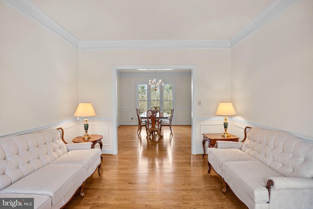 living room with light wood-style floors, wainscoting, crown molding, and an inviting chandelier