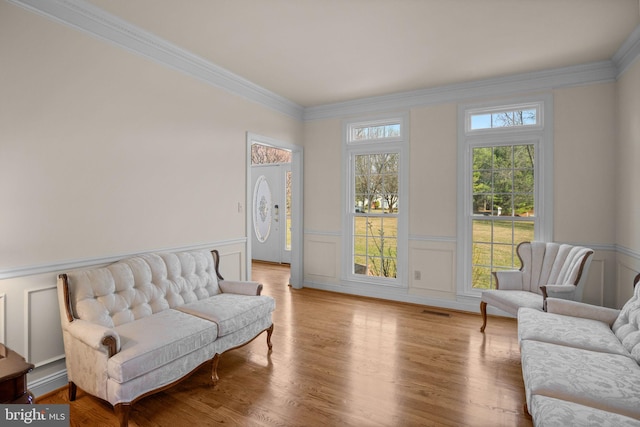 sitting room featuring light wood-type flooring, visible vents, wainscoting, and crown molding