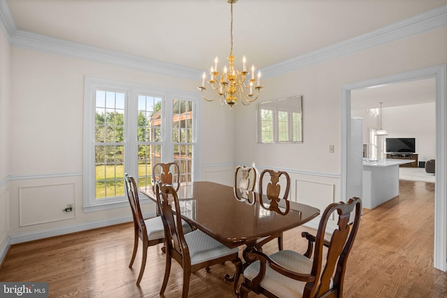 dining area with crown molding, a chandelier, a wainscoted wall, light wood-style floors, and a decorative wall