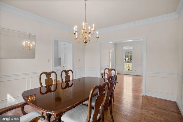 dining area with an inviting chandelier, crown molding, wood finished floors, and a wainscoted wall