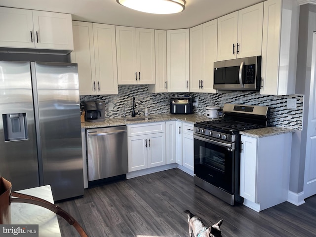 kitchen with white cabinetry, stainless steel appliances, sink, light stone counters, and dark hardwood / wood-style floors