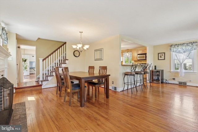 dining area with an inviting chandelier, light wood finished floors, a brick fireplace, baseboards, and stairway