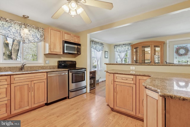 kitchen with light brown cabinetry, a sink, light wood-style floors, stainless steel appliances, and a ceiling fan