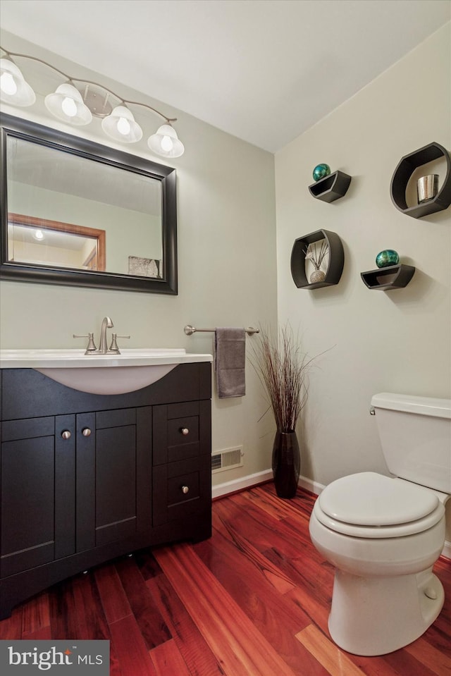 bathroom with toilet, baseboards, visible vents, and wood finished floors