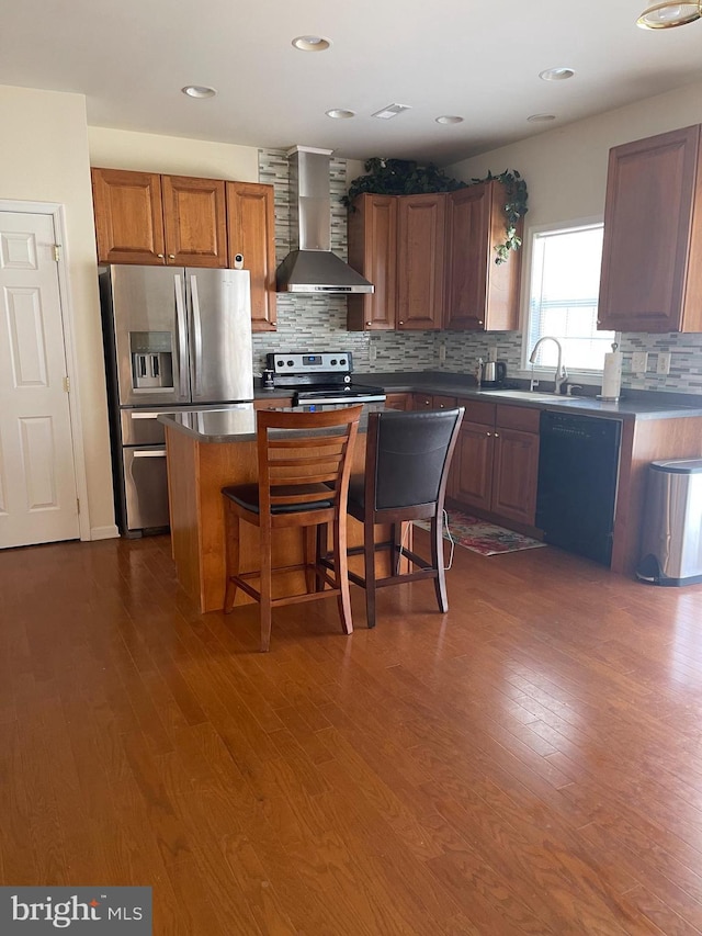 kitchen featuring wall chimney range hood, sink, a breakfast bar, appliances with stainless steel finishes, and a center island