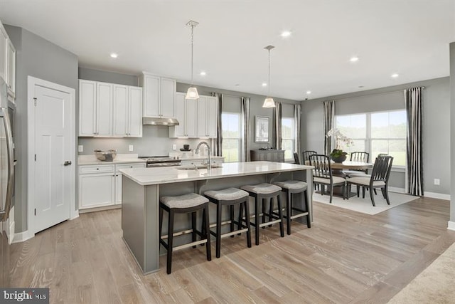 kitchen featuring white cabinetry, an island with sink, sink, a kitchen breakfast bar, and hanging light fixtures