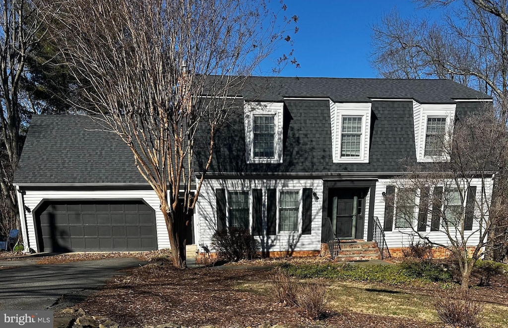 colonial inspired home with a garage, a shingled roof, and driveway