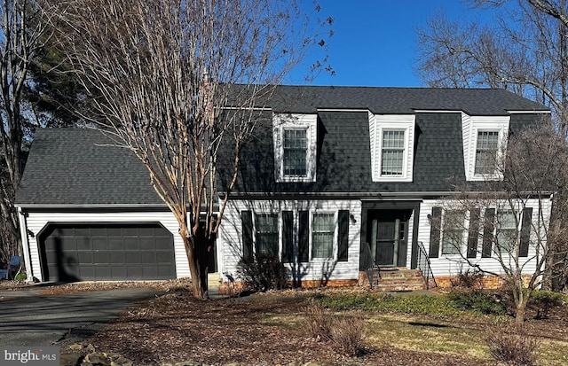 colonial inspired home with a garage, a shingled roof, and driveway