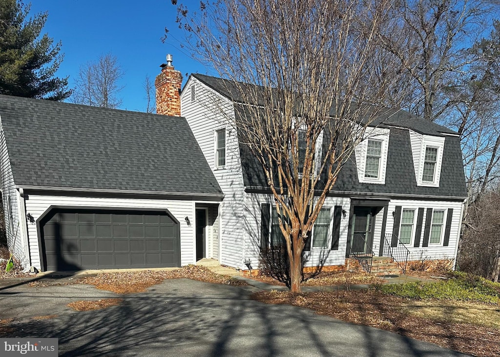 view of front facade featuring a garage, roof with shingles, driveway, and a chimney