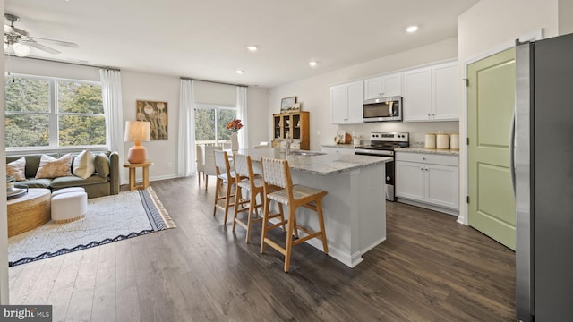 kitchen featuring appliances with stainless steel finishes, white cabinetry, light stone counters, a center island with sink, and dark hardwood / wood-style flooring