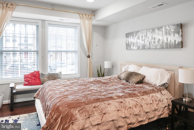 bedroom featuring baseboards, multiple windows, visible vents, and wood finished floors