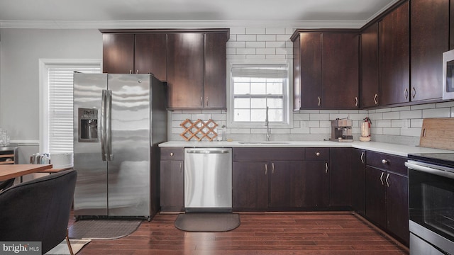 kitchen with stainless steel appliances, dark wood-style flooring, a sink, light countertops, and crown molding