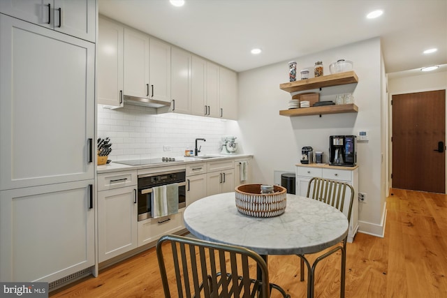 kitchen with sink, white cabinets, black electric stovetop, stainless steel oven, and light hardwood / wood-style floors